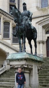 a boy stands in front of a knight on horseback statue