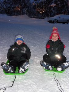 A girl and boy sit on green sledges in the snow