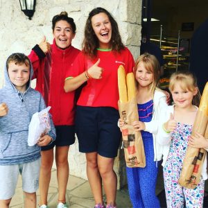 Three children hold bags of bread and croissants after helping Eurocamp couriers buy breakfast for the kids club
