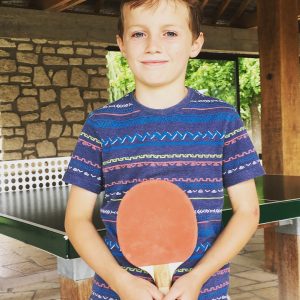 A young boy holds a table tennis bat at a campsite