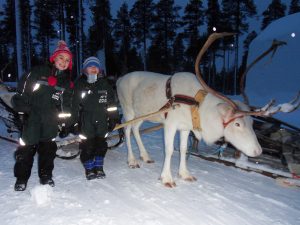 A boy and girl stand next to a white reindeer in the snow in Lapland